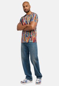 Multifarvet t-shirt med korte ærmer og abstrakte mønstre, kombineret med lyseblå jeans med lige ben og farverige sneakers med mønster.