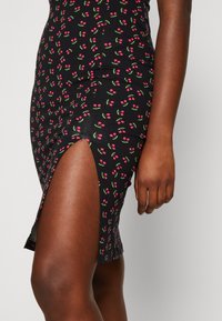 Schwarzes Kleid mit figurnaher Passform, ausgestattet mit einem kleinen Seitenschlitz, ganzflächigem Muster aus rosa und grünen Kirschen, weicher Stoffstruktur.