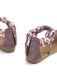 Purple faux leather sandals with a floral braided strap and a zipper detail at the back. Flat sole with a textured surface.