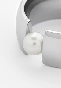 Bracciale d'argento con una perla bianca tonda e liscia, caratterizzato da un design moderno e geometrico con dettagli lucidi e un'apertura a clip.