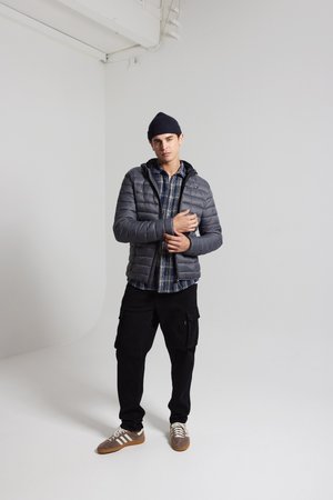 Gray padded jacket with a zipper and hood, over a blue plaid shirt, paired with black cargo pants and brown sneakers with white stripes.