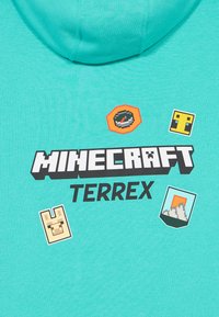 Türkiz kapucnis pulcsi Minecraft TERREX felirattal és pixel művészeti ikonokkal, beleértve egy iránytűt, lámát, hegyet és négyzet alakú arcot.