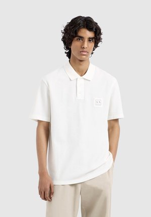 Polo bianco realizzato in un tessuto texturizzato e traspirante, con maniche corte, colletto a punta e una piccola etichetta con logo sul petto.
