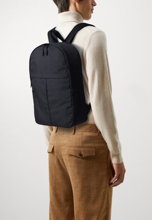 Black fabric backpack with a rounded top, two adjustable straps, and exterior zipper pocket. Smooth texture, simple design, and sleek shape.
