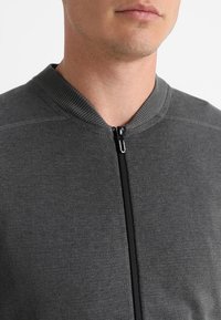 Giacca grigia con zip e colletto a costine, dotata di una zip centrale e una morbida trama a maglia. Il design è semplice e funzionale.