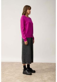 Fuchsia gebreide trui, losse pasvorm, ronde halslijn, gecombineerd met hoge taille zwarte wijde jeans en zwarte veterschoenen.