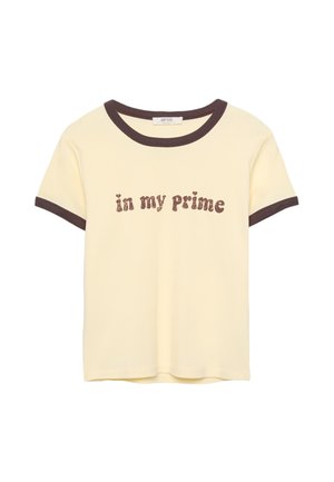 Lys gul t-shirt med brun ribbet halsudskæring og ærmer, med teksten "in my Prime" i en tekstureret brun skrift. Materiale: bomuld.