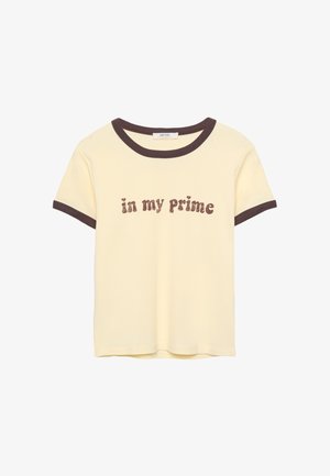 Lys gul t-shirt med brun ribbet halsudskæring og ærmer, med teksten "in my Prime" i en tekstureret brun skrift. Materiale: bomuld.