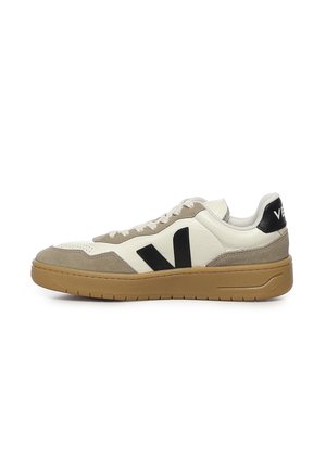 Sneaker basse en suède beige, tige en cuir blanc, logo "V" noir sur le côté, semelle en caoutchouc gomme, et languette de talon noire avec texte blanc.
