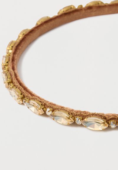 Ruskea kangaspanta, jossa kullanväriset metalliset koristeet ja kirkkaat, marquise-leikatut strassit reunassa. Sileä pinta.