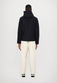 Černá mikina s kapucí volného střihu v kombinaci s krémovými cargo kalhotami se bočními kapsami a texturovanou tkaninou. Černé a bílé boty.