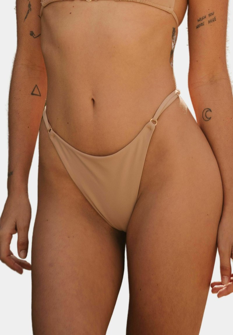 Bikini dolna część w jasnobeżowym kolorze, z cienkimi bocznymi paskami, w wysokim kroju nogawek oraz minimalnym pokryciem, o gładkiej fakturze.