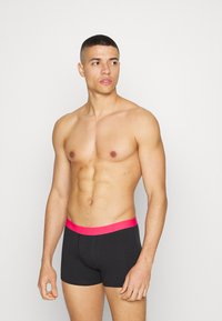 Black boxer shorts with a wide, bright pink waistband, featuring a fitted design and soft fabric, displayed on a male model.