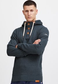 Sötét szürke kapucnis pulóver, gombos nyakkal, kr�ém színű zsinórokkal, barna részletekkel és logóval ellátott patch-el az ujjon. Puha tapintású és lazán illeszkedő fazon.