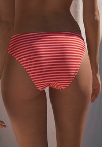 Culotte da bikini a righe rosse e bianche con una texture liscia e copertura media. Presenta taglio pulito e un design semplice della vita.