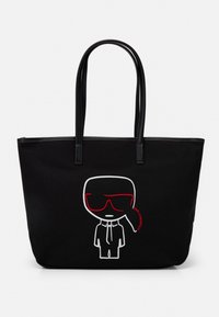 Svart tote-väska med svarta läderhandtag, prydd med en broderad tecknad figur i vitt och rött som bär solglasögon och kostym.