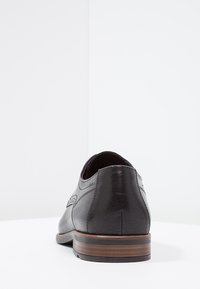 Black leather shoe with a smooth finish, featuring decorative stitching, a rounded toe, and a brown wooden heel accent.