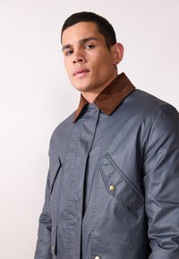 Gray waterproof jacket with a brown corduroy collar, snap buttons, and front flap pockets, showcasing a smooth texture and tailored fit.