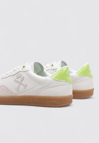 Baskets blanches avec accents verts, en cuir et en daim, dotées d'une semelle en caoutchouc et d'un logo en relief sur le côté.