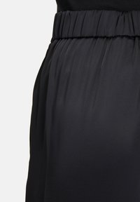 Zwart, lichtgewicht stof met een geplooide elastische tailleband. Gladde textuur; ontwerp heeft vloeiende draping en een minimale glans.