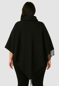 Poncho nero con colletto alto, caratterizzato da un bordo frangiato diagonale sull'orlo e una texture liscia. Design ampio per il massimo comfort.