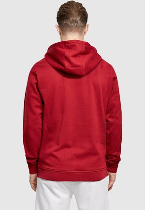 Roter Kapuzenpullover mit weichem Stoff, langen Ärmeln und geripptem Saum. Die Kapuze ist auffällig und ohne sichtbare Muster.