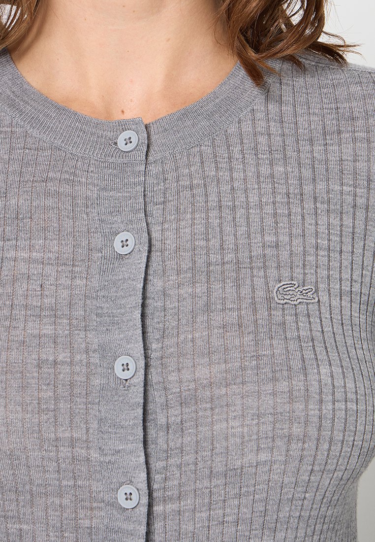 Grauer gerippter Cardigan aus weichem Material, mit rundem Ausschnitt, mittelgroßen grauen Knöpfen und einem kleinen Logo auf der linken Seite.