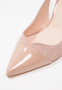 Ballerine à bout pointu en cuir verni beige et daim avec un détail de bord festonné.