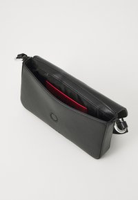Pochette en cuir noir au design élégant. L'intérieur révèle une poche rouge. Dotée d'une fermeture à glissière et d'un accent en logo circulaire.