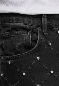 Melna džinsu auduma bikses ar dimanta raksta diega šuvēm un nelieliem pērlītēm, kuras parāda priekšējo kabatu un jostas cilpu ar zīmola birku.