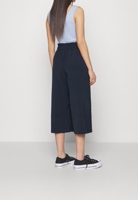 Blue ribbed tank top paired with high-waisted, wide-leg navy culottes and black sneakers, featuring a comfortable elastic waistband.