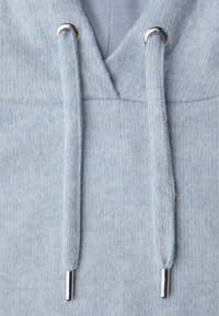 Lyseblåt hættetrøjestof med mønster i struktur. Indeholder sølvfarvede øjer og snore til justering. Nærbillede af materialets detaljer.