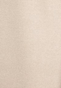Tessuto in maglia di colore beige chiaro con una texture fine e un motivo sottile. La superficie è liscia con una trama uniforme.