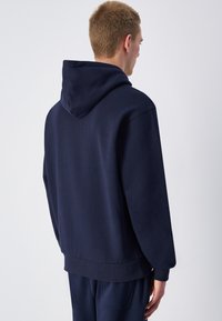 Felpa con cappuccio di colore blu navy, dotata di tasca a marsupio, polsini e fondo a coste. Presenta un cappuccio con cordino e una texture morbida e liscia.