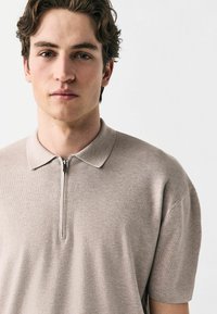 Beige polo t-shirt lavet af struktureret strikstof, med lynlås, korte ærmer og klassisk krave.