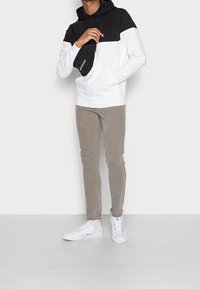 Schwarz-weißer Kapuzenpullover mit Kängurutasche. Hellgraue schmal geschnittene Hose und weiße Sneaker runden das Outfit ab.