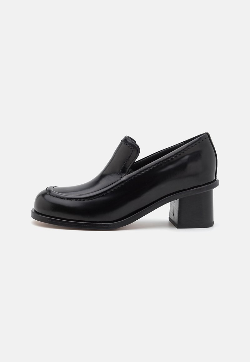 Black patent leather loafers with a rounded toe, raised stitching detail, and a block heel. Smooth texture with minimalistic design.