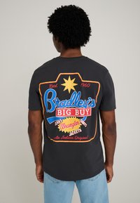 Black cotton t-shirt featuring a colorful print on the back with text elements. The design includes a yellow star and multicolored accents.