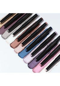 Dix crayons d'ombre à paupières noirs disposés en diagonale sur une surface blanche avec des nuances estompées en or, argent, blanc, bronze, bleu, violet et rose.