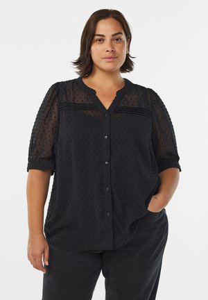 Zwarte, doorzichtige blouse met korte puffmouwen, gestructureerd stippenpatroon, knopen aan de voorkant en een V-halslijn. Zacht materiaal met een losse pasvorm.