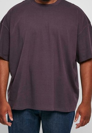 Dunkelviolettes, übergroßes Baumwoll-T-Shirt mit Rundhalsausschnitt und kurzen Ärmeln, kombiniert mit blauen Denim-Jeans. Glatte Textur, lässige Passform.