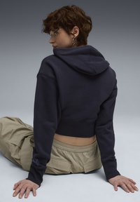 Afskåret navy hoodie med en frontlomme og hætte, parret med lysebeige cargo bukser. Blød tekstur og ribbede manschetter synlige.