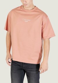 Camiseta grande de color rosa claro hecha de algodón, con el logo de Calvin Klein Jeans en blanco en el pecho, manga corta y cuello redondo.