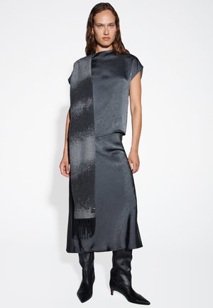 Ensemble en deux pièces en satin dans des nuances de noir et de gris, comprenant un haut texturé et une jupe fluide, associé à des bottes pointues jusqu'aux genoux.