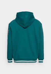 Tannengrüner Kapuzenpullover mit langen Ärmeln, weißen gestreiften Bündchen und Saum, mit einem Aufnäher mit der Nr. 5 auf der Rückseite des linken Ärmels.