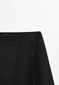 Jupe plissée noire avec une taille ajustée et une fermeture éclair latérale sur un fond blanc uni.
