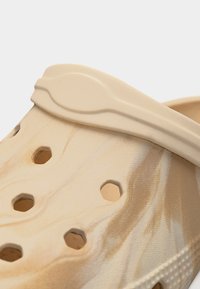 Κοντινό πλάνο μπεζ μαρμάρινης παντόφλας χωρίς κορδόνια με οπές αερισμού και ρυθμιζόμενο λουράκι στη φτέρνα.