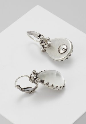 Srebrne kolczyki z kroplą z przezroczystymi owalnymi kamieniami osadzonymi w misternych oprawkach na białym tle.