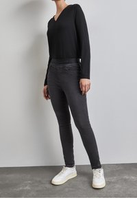 Svart långärmad topp med V-ringning, matchad med grå tajta jeans med en diskret denimtextur och en slät midja. Vita sneakers.