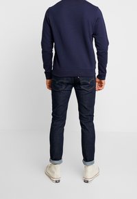 Laivaston sininen collegepaita pyöreällä kaula-aukolla, yhdistetty tummansinisiin farkkuihin. Rento valkoinen tennarit, joissa käännetyt lahkeet. Yksinkertainen, toiminnallinen muotoilu.